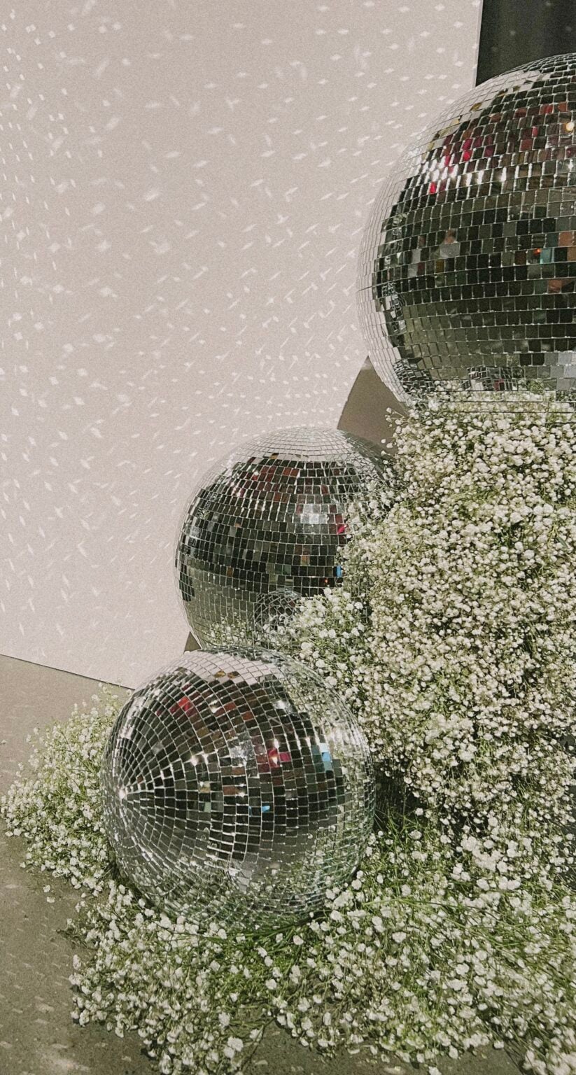 A close-up, vertical shot of three large, reflective disco balls nestled within a dense arrangement of white baby's breath flowers and green foliage.