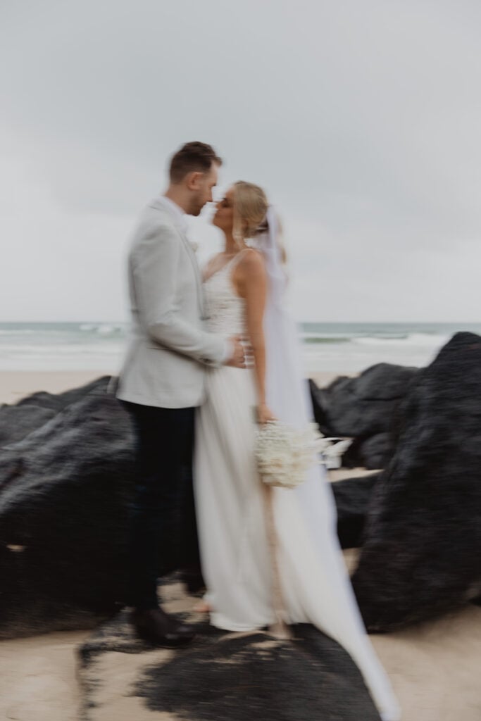 A blurry, motion-filled photograph of a bride and groom embracing intimately on a beach.