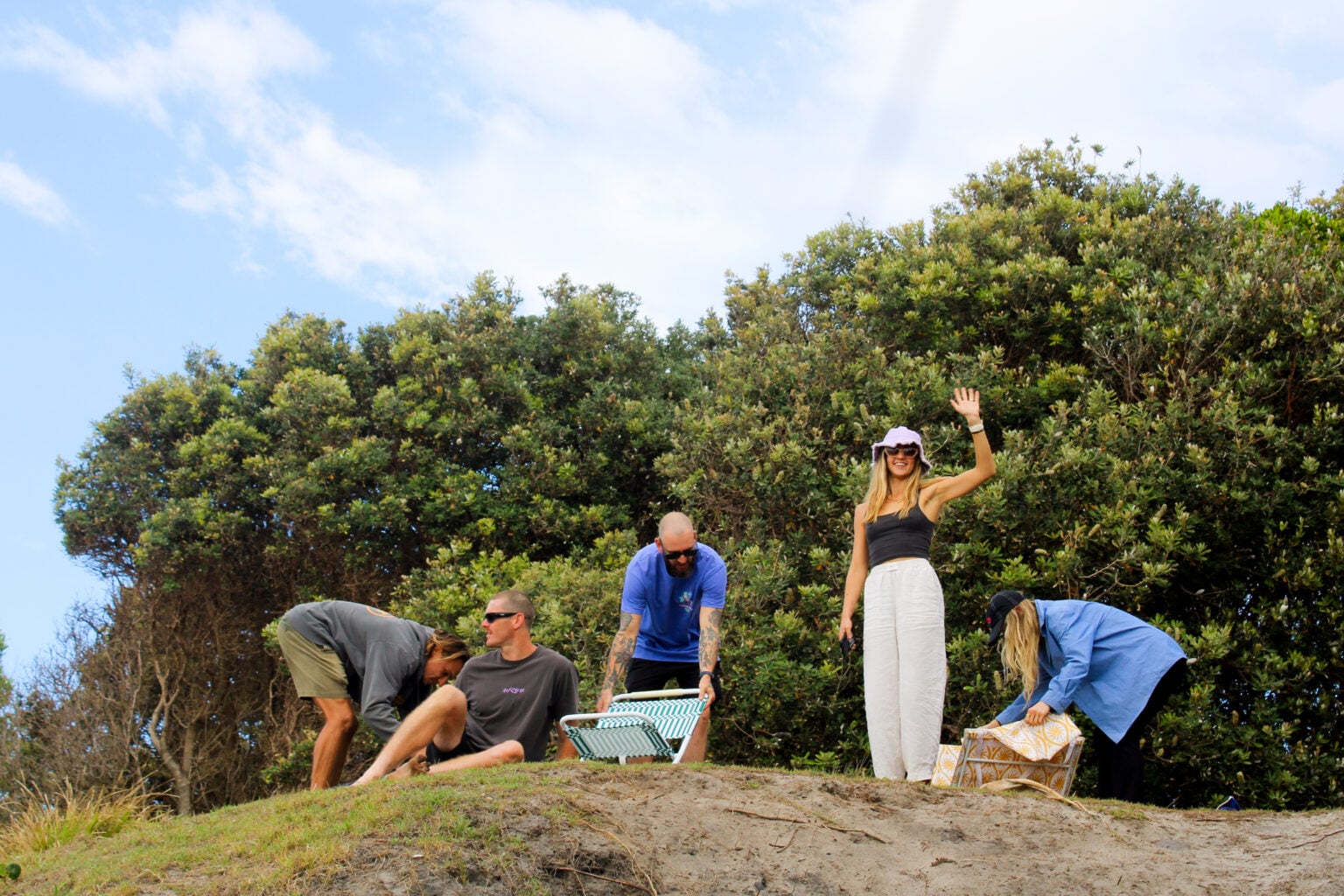 A group of five people gathering on a grassy dune with dense trees in the background