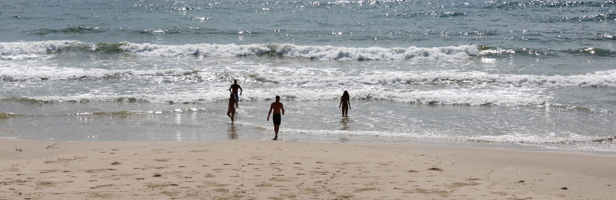 Four people walking into the ocean surf on a sunny day