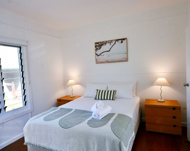 A room with two rolled white towels at the foot and a black and white striped bolster pillow.