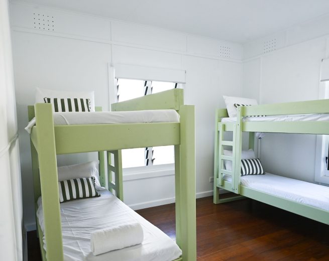 A bright, minimalist bedroom featuring two sets of light sage green wooden bunk beds.