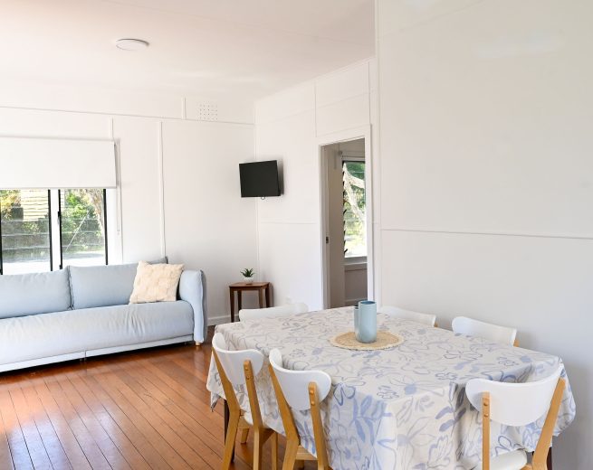 A bright, minimalist living and dining area with white walls and polished wooden floors.