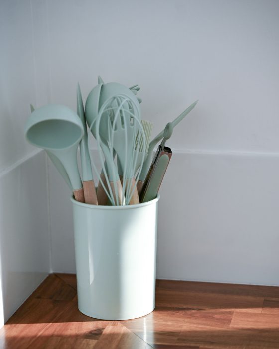 A close-up vertical shot of a collection of kitchen utensils in a light mint green holder.