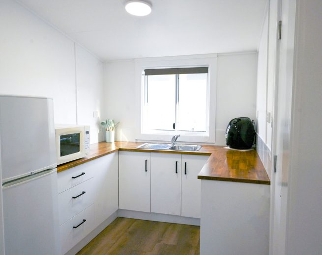A bright, minimalist U-shaped kitchen with white walls and warm wood-look flooring.
