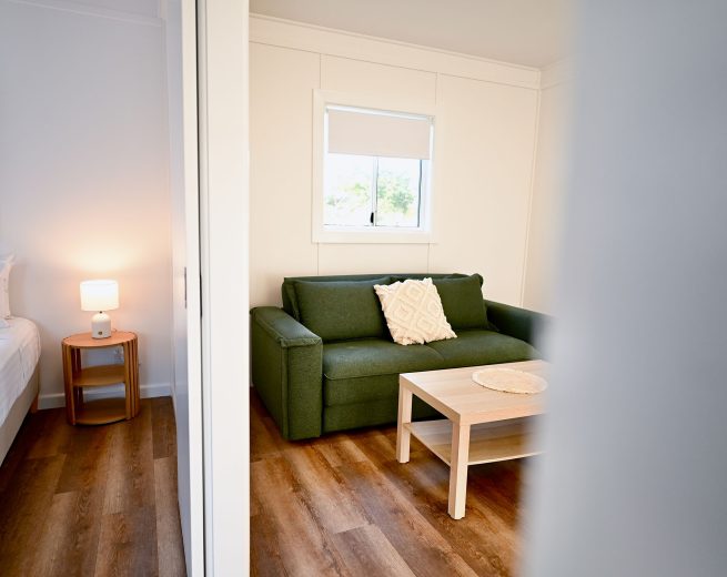 An interior shot of a living area and a bedroom viewed through a blurred white doorway on the right.