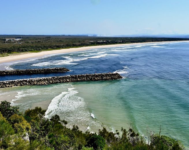 A high-angle, panoramic view of a long, sandy beach and coastline on a bright sunny day
