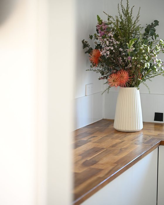 A close-up vertical shot of a kitchen countertop with a vase of flowers, viewed through an out-of-focus white doorway or wall on the left.