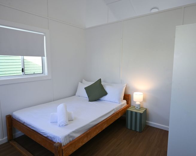 The bed is covered in white striped linens with a single dark olive green decorative throw pillow nestled among the white pillows.