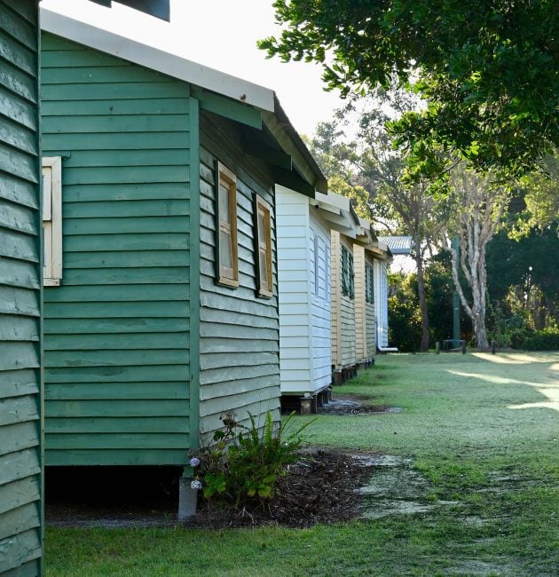 A line of small, rustic wooden cabins or shacks, viewed from a low angle.