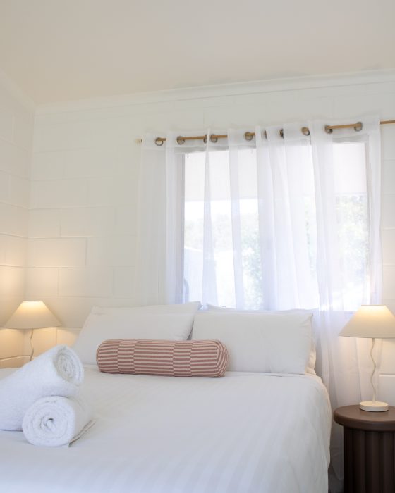 A bright bedroom featuring a white bed with rolled towels and a striped bolster pillow