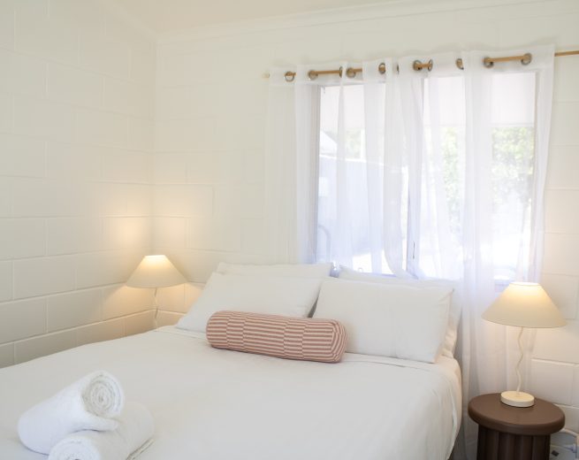 A minimalist bedroom setup featuring a white bed with a pink striped bolster pillow