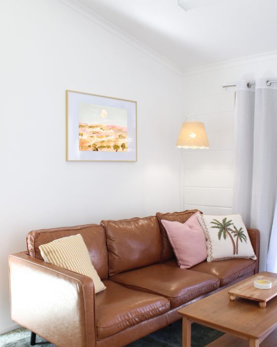 A brown leather sofa with decorative pillows sits in a bright living room