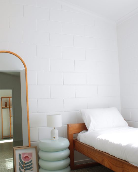 A modern bedroom scene featuring a wooden bed frame with white linens