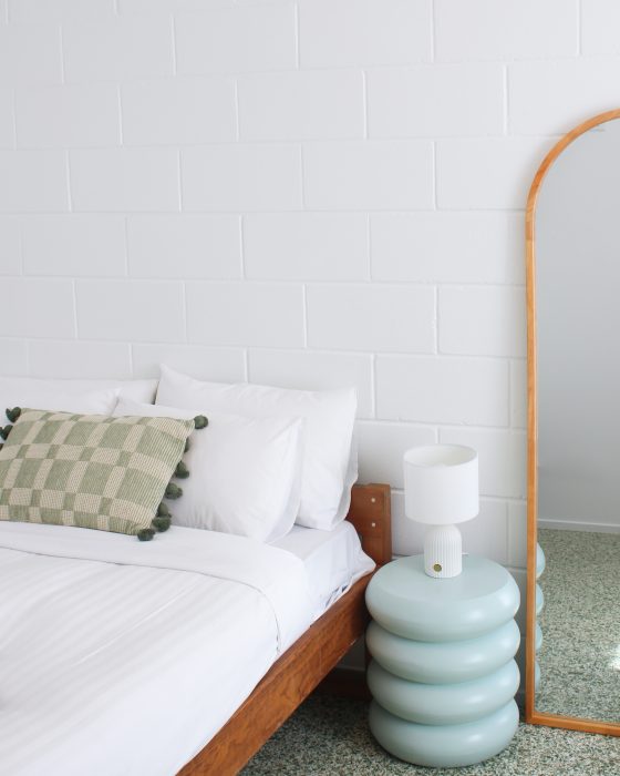 A bright bedroom featuring a wooden bed frame with white linens and a green chequered decorative pillow.