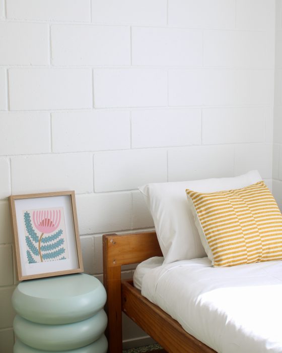 A modern bedroom scene featuring a wooden bed frame with white linens and a yellow-and-white striped pillow.