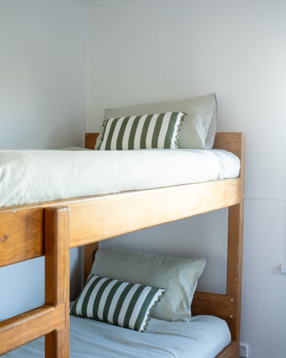 Wooden bunk beds with light sage green linens and green-and-white striped accent pillows against a white wall.