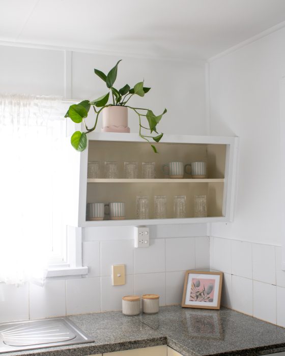 A bright kitchen corner featuring an open white cabinet with glasses and striped mugs