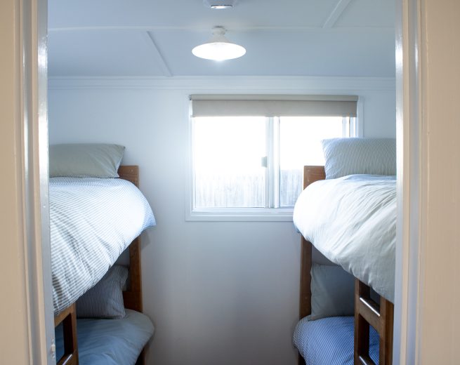 A bedroom viewed through a doorway, containing two sets of wooden bunk beds with blue and white striped bedding