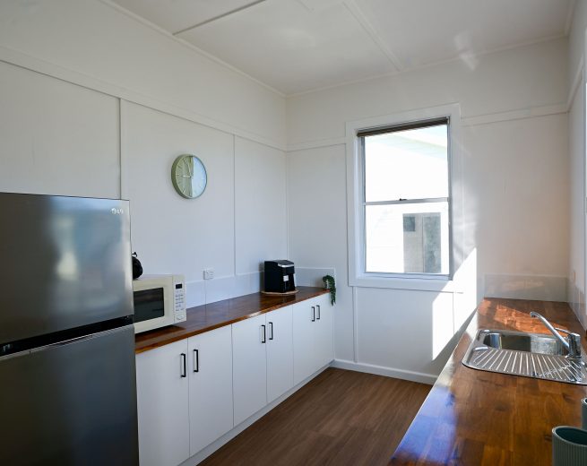 A bright, modern kitchen with white walls and a long, glossy, wooden butcher-block countertop.