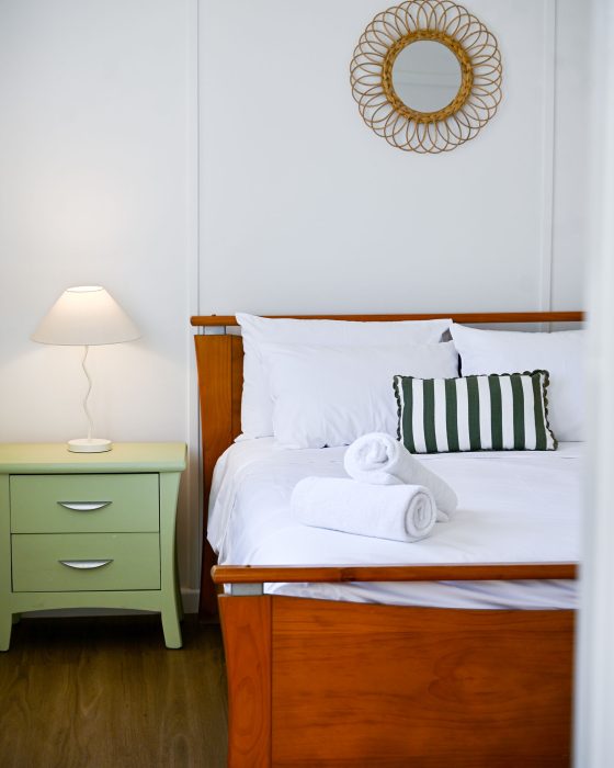 Above the bed on the white wall, a small, circular mirror with a decorative rattan or wicker sunburst frame is mounted.
