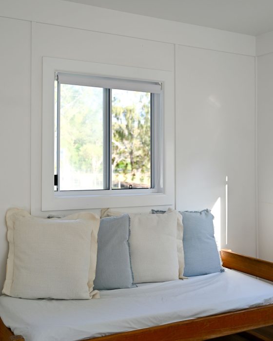 A vertical interior shot of a bright room with white walls, focusing on a wooden daybed or futon.