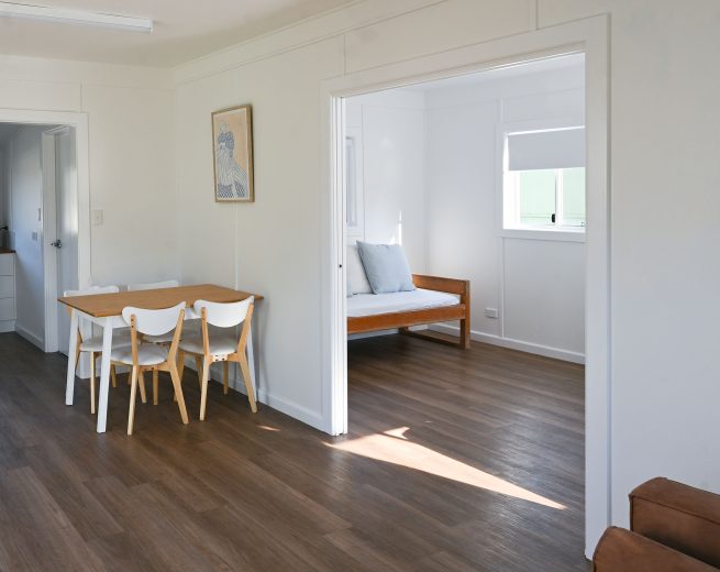 An interior shot of a bright, open-plan living area with warm brown wood-look flooring and white walls.
