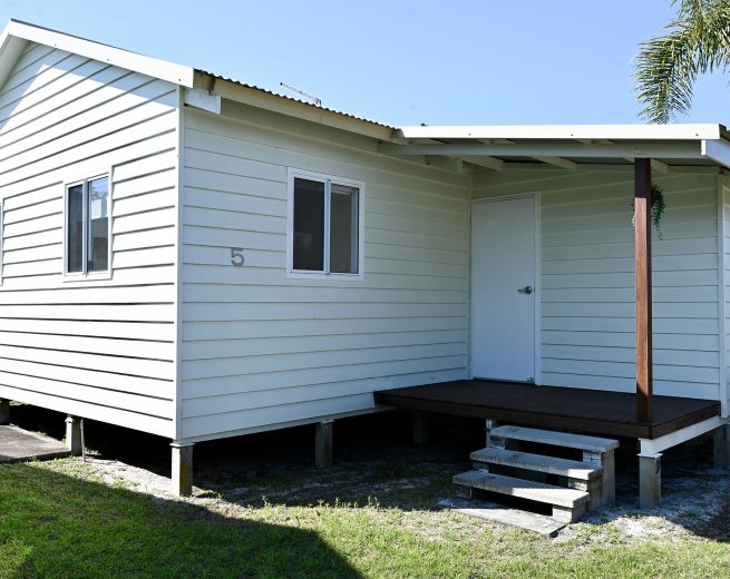 The exterior of a small, elevated vacation cabin or bungalow, numbered '5', on a bright sunny day.