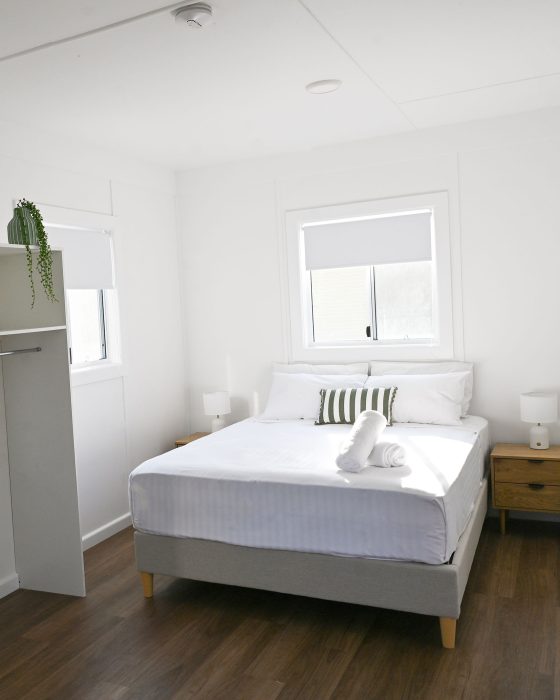 A bright, minimalist bedroom with white walls and a warm brown wood-look floor.