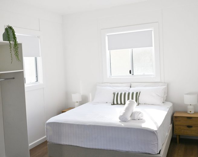 A bright, minimalist bedroom with white walls and a warm brown wood-look floor.
