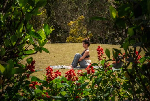 young woman in meditative pose on a lawn framed by flowers